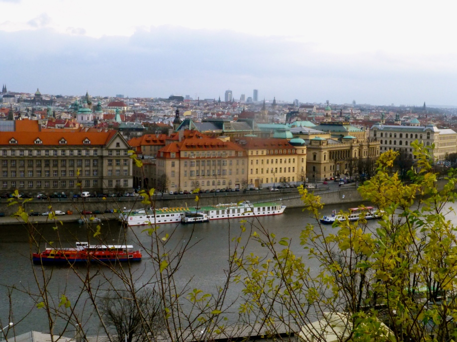 Prague - River flanked by rows of grossly grand blocks.  Painted soft orange, deep yellow, soft green or cream - all sporting the uniform red-clay roof tiles.